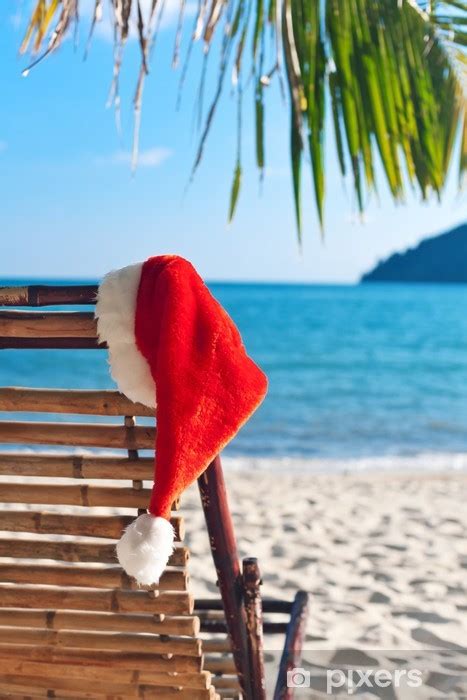 Naklejka Red Hat Santa wiszący na krześle na plaży pod palmą PIXERS PL