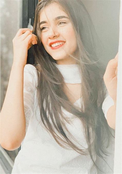 A Woman With Long Hair Standing Next To A Window Holding A Cell Phone