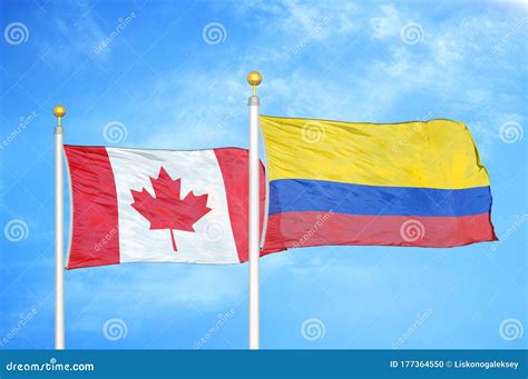 Canada And Colombia Two Flags On Flagpoles And Blue Cloudy Sky Stock