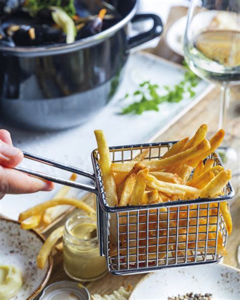 Une main tient des frites fraîchement préparées dans un panier métallique