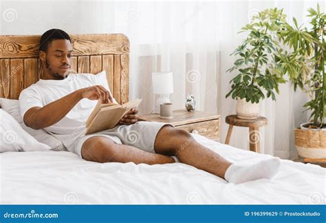 African American Man Reading Book Lying In Bed At Home Stock Image