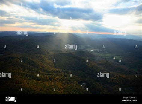 Crepuscular rays beam down from clouds above onto Pinnacle Mountain covered in fall foliage near ...