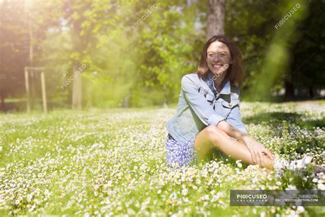 Smiling young woman sitting in park — backlit, daisies - Stock Photo ...