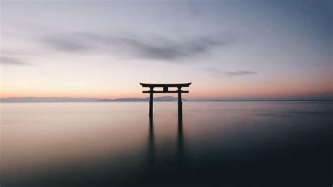 a large body of water with a small structure in the middle of it at sunset