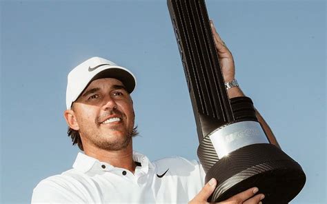 A Man Holding A Trophy In His Right Hand And Wearing A White Shirt With