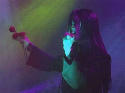 A Woman With Long Hair Holding A Microphone In Front Of Purple And Green Light Beams