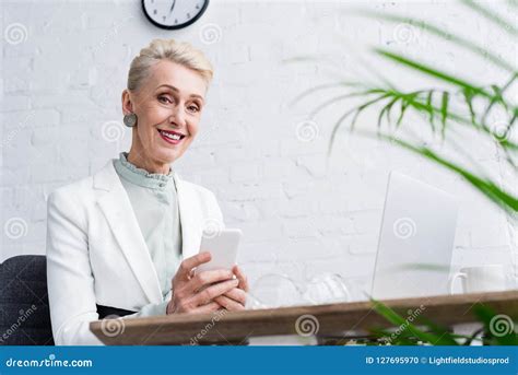 Happy Senior Businesswoman Using Smartphone At Workplace Stock Photo