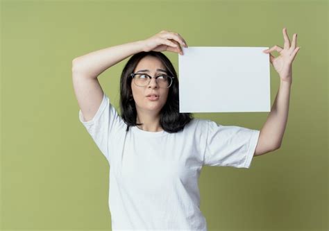 Impresionada joven bastante caucásica con gafas sosteniendo y mirando