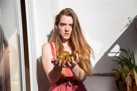 Premium Photo Portrait Of Young Woman Holding Kiwis Against Wall