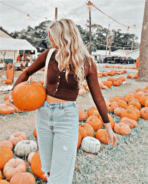 A Woman Standing In Front Of Pumpkins With Her Hands Behind Her Back To