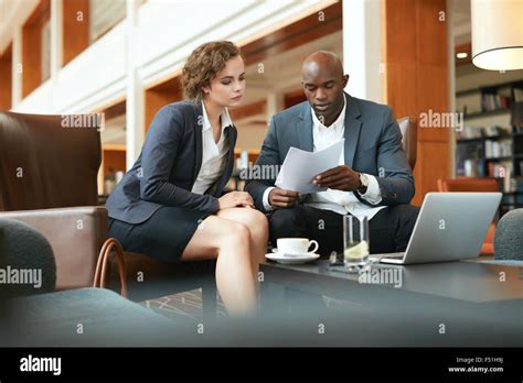 Two Young Business People With Papers Meeting In Hotel Lobby African