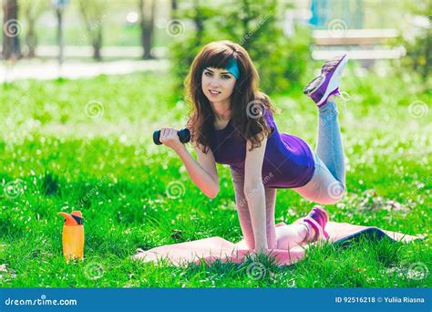 Fitness Girl In The Park And Engaged In Various Exercises With Dumbbell