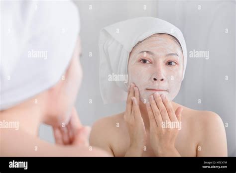 Woman Applying Mask On Her Face And Looking In The Mirror In The