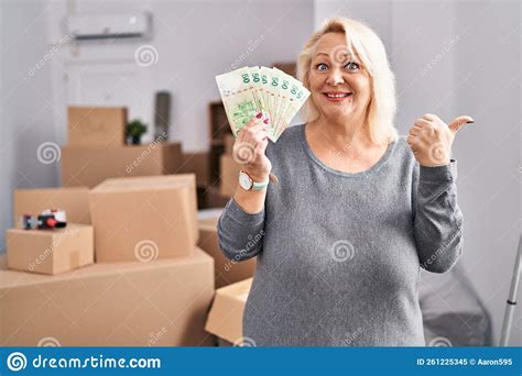 Middle Age Caucasian Woman Moving To A New Home Holding Hong Kong Dollars Pointing Thumb Up To