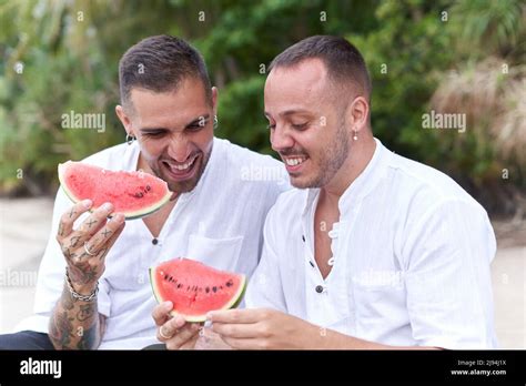 Two Gay Men Sitting On A Beach While Smiling And Holing A Piece Of Watermelon Stock Photo Alamy