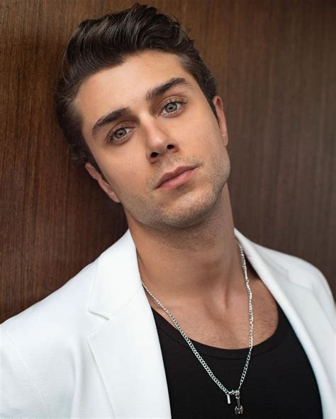 A Man In A White Jacket Leaning Against A Wooden Wall With His Hand On