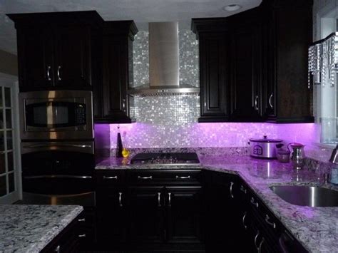 A Kitchen With Black Cabinets And Purple Lights On The Backsplash Is