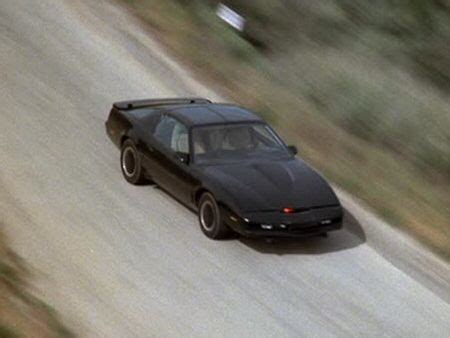 a black car driving down a road next to trees