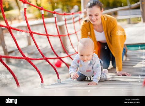 Mother watching her baby girl playing on playground Stock Photo - Alamy