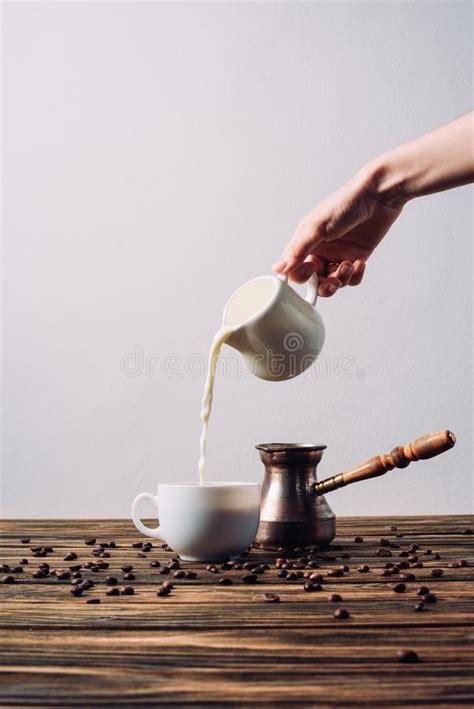 Cropped Shot Of Woman Pouring Milk Into Coffee On Rustic Stock Image