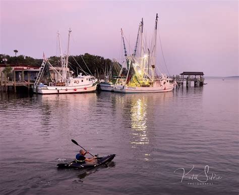 a person in a kayak paddling on the water next to several docked boats