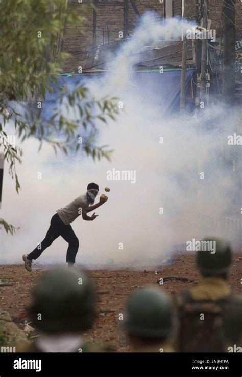 A Masked Kashmiri Muslim Protester Throws Back An Exploded Teargas