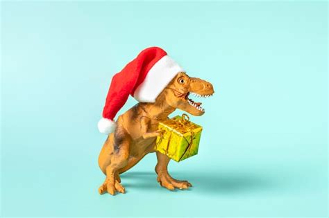 Premium Photo Dinosaur Rex In Red Santa Claus Hat Holds Golden Gift