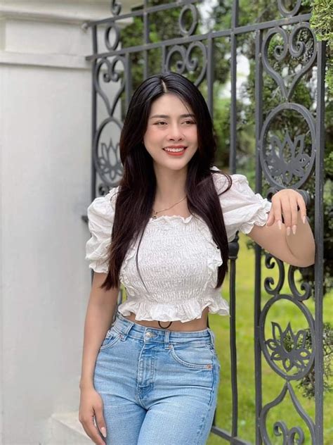 A Woman Standing Next To A Gate Wearing Jeans And A White Top With