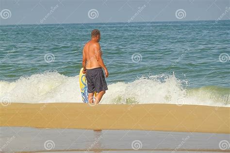 Shirtless Man Walking On A Sandy Beach Getting Ready To Surf In The Ocean Editorial Image