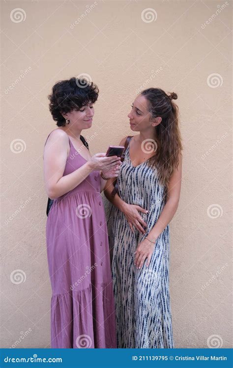 Beautiful Lesbian Couple Wearing Long Dresses Using A Mobile In The Street Stock Image Image
