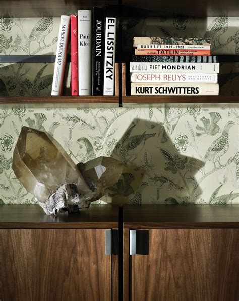 A Book Shelf With Books And An Object On It Next To A Wallpapered Wall