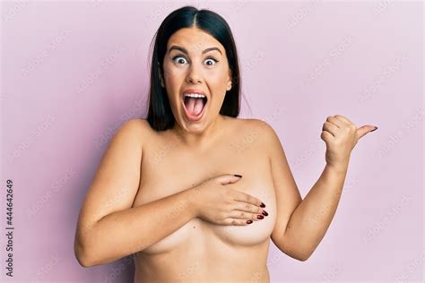 Beautiful Brunette Woman Standing Naked Covering Breasts Pointing Thumb Up To The Side Smiling