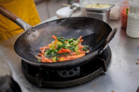 Premium Photo | Cook fries vegetables in a wok pan on fire Chef is ...