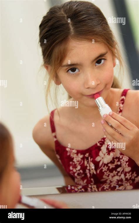 Cute little girl gently applying makeup while looking at her reflection ...