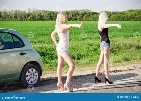 Two Blonde Girls Standing Near Their Broken Car And Hitchhiking Stock