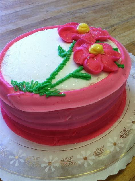 A Cake With Pink Frosting And Flowers On It Sitting On A Plate In Front