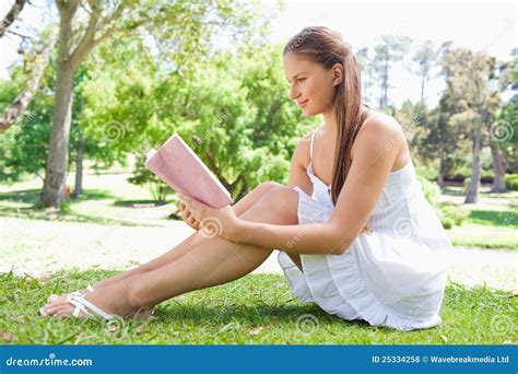 Side View Of A Woman Sitting On The Lawn While Reading A Book Stock