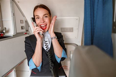 Joyful Female Flight Attendant Talking On Telephone In Airplane Stock