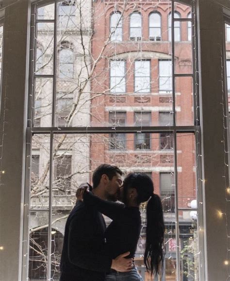 A Man And Woman Kissing In Front Of A Window