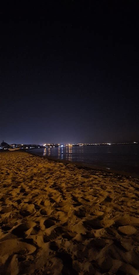 The Beach Is Covered In Sand At Night With Lights Shining On The Water