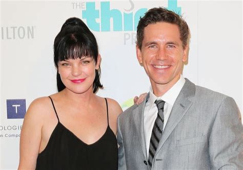 A Man And Woman Standing Next To Each Other In Front Of A White Wall