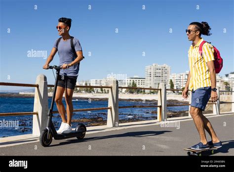 Happy Biracial Gay Male Couple Riding Scooter And Skateboard On