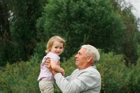 公園で散歩中に楽しい祖父と孫の赤ちゃん 幸せな家族 夏の日に2歳の女の子を抱き締める老人おじいちゃん 笑顔で孫娘と一緒に時間を過ごすシニア男性