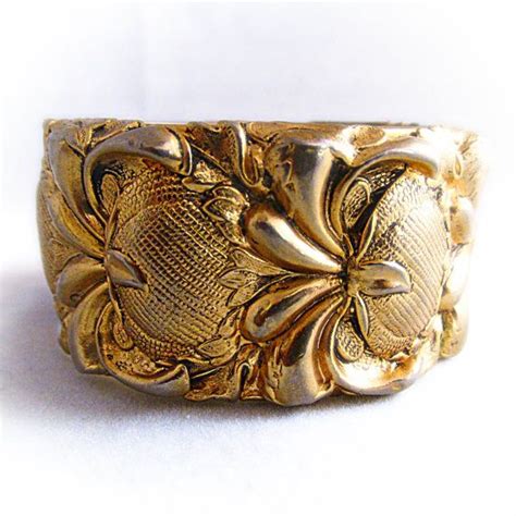 A Close Up Of A Gold Ring On A White Surface With Flowers And Leaves In