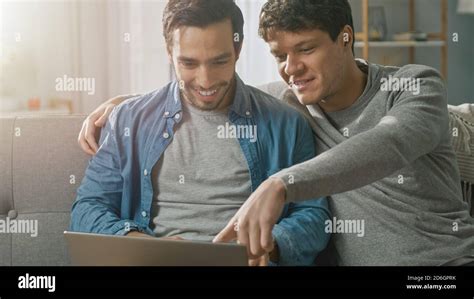 Adorable Male Gay Couple Spend Time At Home They Sit On A Sofa And Use The Laptop They Browse