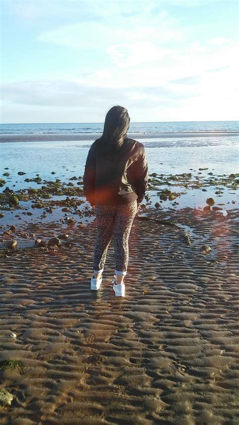 A Woman Standing On Top Of A Sandy Beach Next To The Ocean With Her