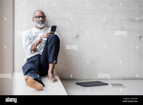 Barefoot Mature Businessman Sitting On Window Sill Looking At