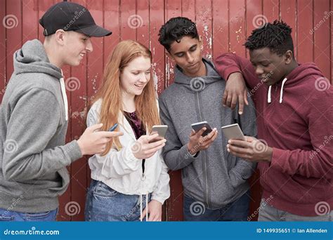 Group Of Teenage Friends Looking At Mobile Phones In Urban Setting