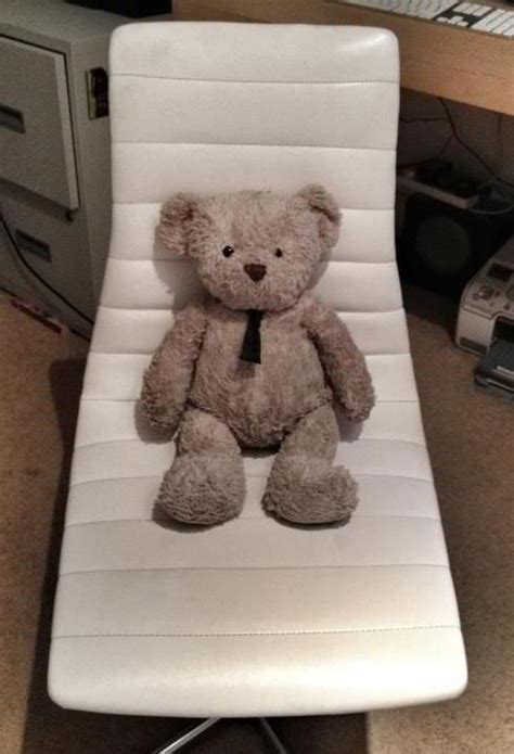 A Brown Teddy Bear Sitting On Top Of A White Chair Next To A Computer Desk