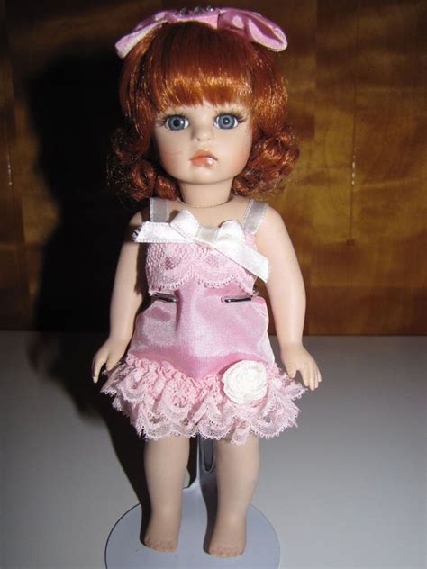 A Doll With Red Hair And Blue Eyes Is Standing On A White Surface